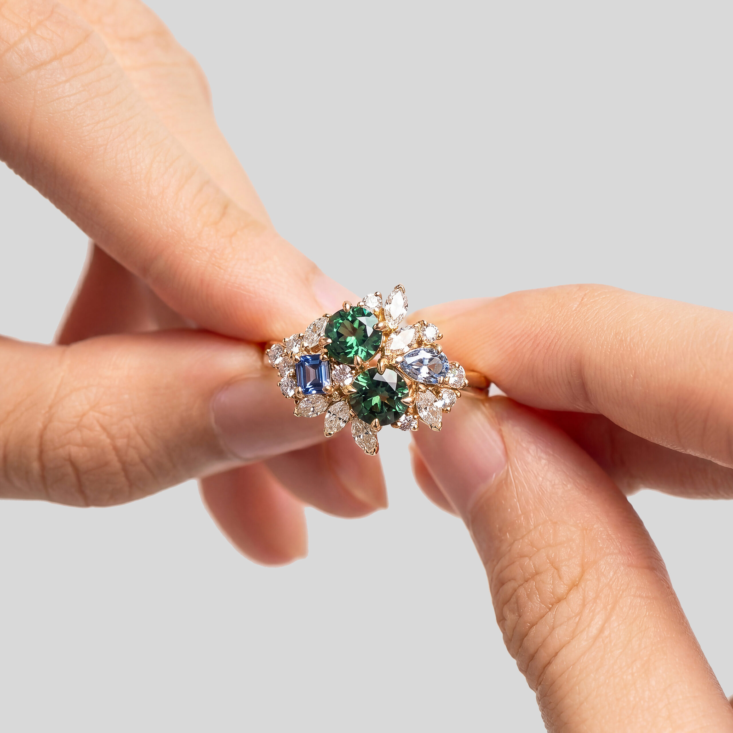 Bague sertie d'une pierre verte entourée de saphirs violets, tenue entre les doigts — Bonnot Paris