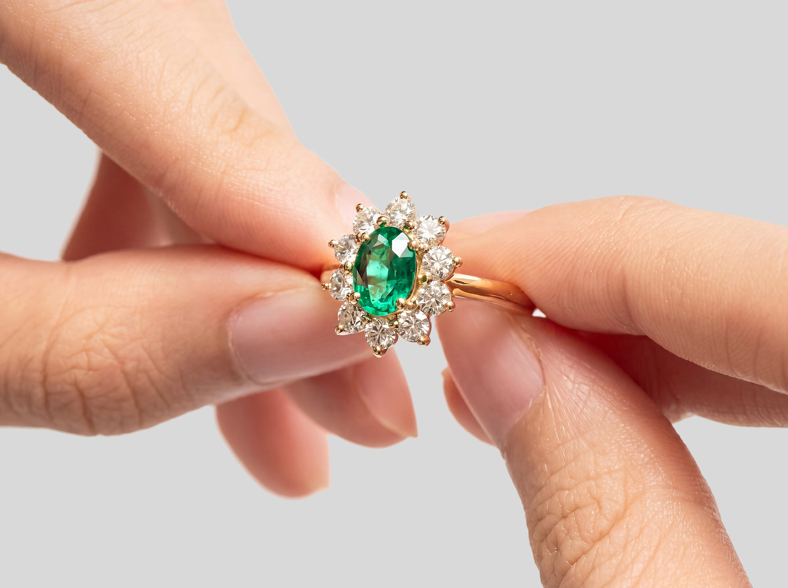 Anello con smeraldo contornato da diamanti tenuto tra due dita — Bonnot Paris